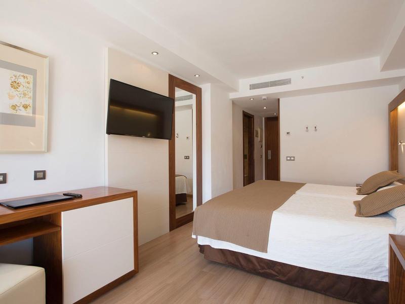 Modern hotel room with double bed, TV, and desk in neutral tones.