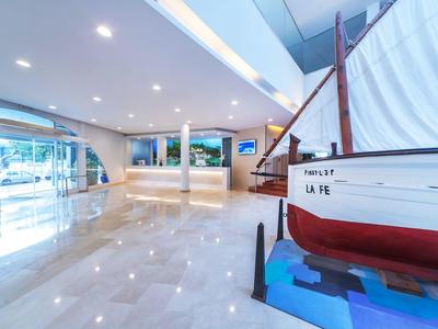 Ingresso dell'hotel luminoso con esposizione di barche, pavimenti in marmo e reception.