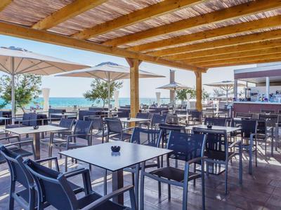 Terrazza coperta con tavoli e sedie, vista sul mare in una giornata di sole.