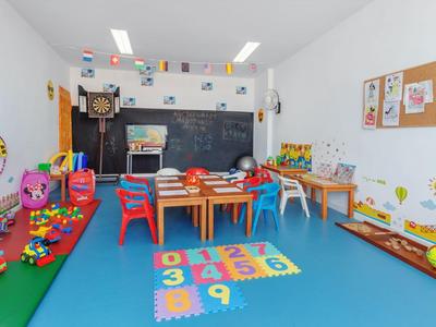 Stanza giochi colorata per bambini con tavoli, sedie, giocattoli e decorazioni murali.