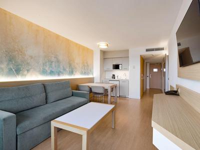 Appartamento moderno con divano, tavolino, cucina attrezzata e TV a parete.