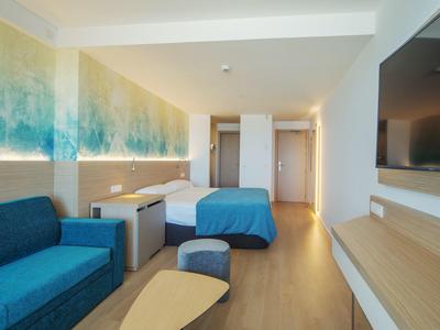 Camera d'hotel moderna con divano blu, letto e grande televisore a schermo piatto.