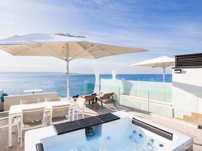 Terrazza moderna sul mare con vasca idromassaggio, lettini e ombrelloni.