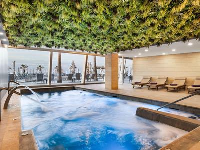 Area benessere moderna con vasca idromassaggio, soffitto verde e vista sulla città attraverso grandi finestre