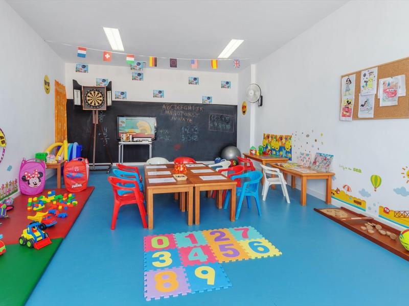 Stanza giochi colorata per bambini con tavoli, sedie, giocattoli e decorazioni murali.