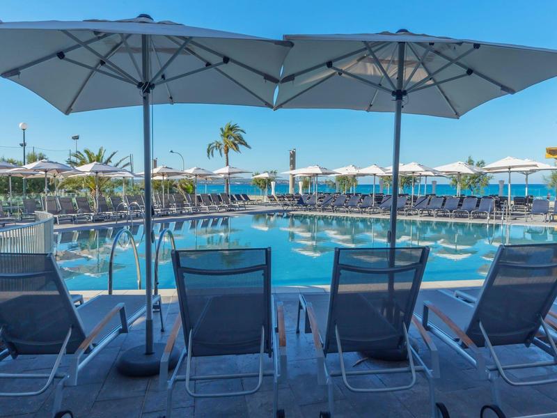 Quattro sdraio sotto ombrelloni accanto a una piscina d'hotel con acqua limpida.