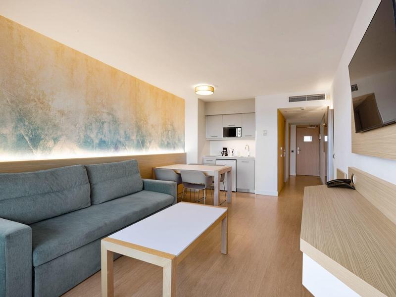 Appartamento moderno con divano, tavolino, cucina attrezzata e TV a parete.