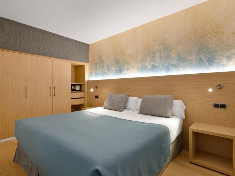 Camera d'hotel moderna con letto grande, mobili in legno e illuminazione d'atmosfera alla parete.