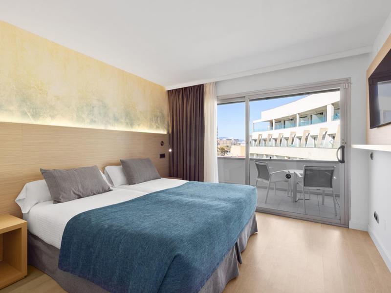 Camera d'hotel moderna con letto matrimoniale, balcone e vista sugli edifici circostanti.