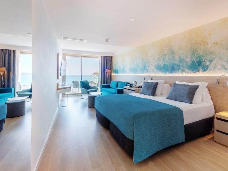 Camera d'hotel moderna con letto matrimoniale, zona salotto e grande finestra con vista mare.