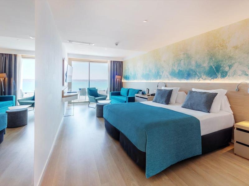 Camera d'hotel moderna con letto matrimoniale, zona salotto e vista sul mare attraverso grandi finestre.