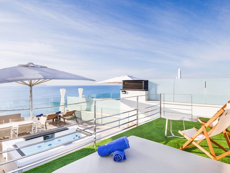 Terrazza sul tetto con sdraio, ombrelloni e vista sul mare con cielo limpido.