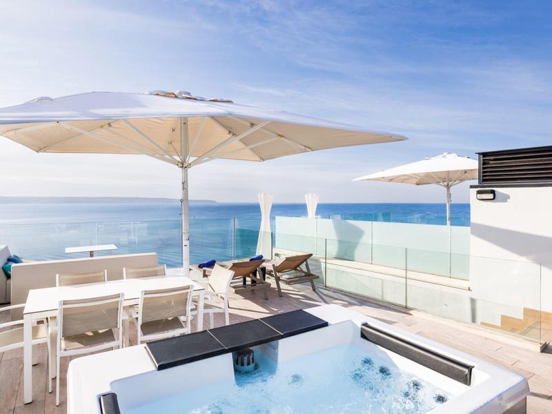 Terrazza moderna sul mare con vasca idromassaggio, lettini e ombrelloni.