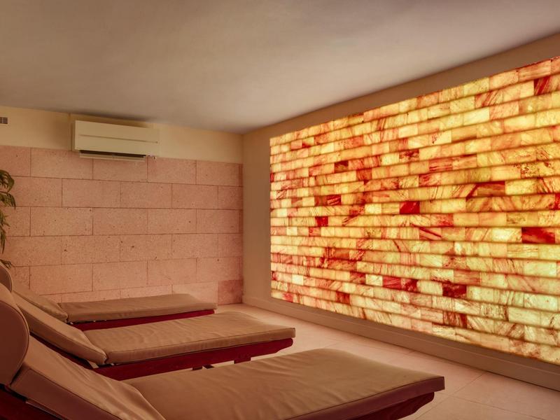 Area relax con lettini e parete illuminata in pietra di sale per il benessere in hotel.