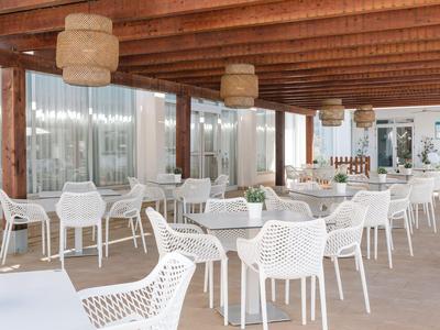 Svítící terasa s bílými židlemi a stoly, dřevěným stropem a velkými okny.