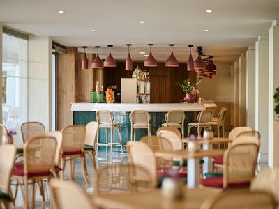 Moderní hotelový bar s židlemi, stoly a dekorativním pultem v pozadí.