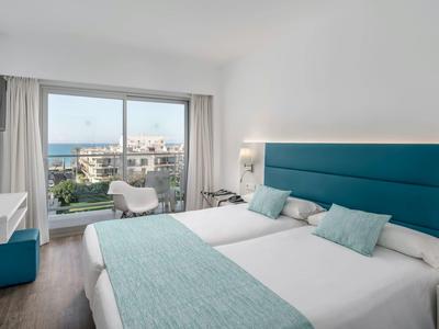 Moderní hotelový pokoj se dvěma jednolůžky, kobercem a výhledem na moře přes velká okna.