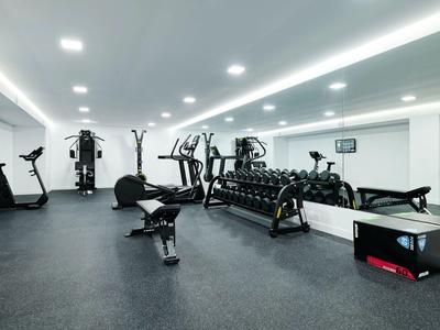 Moderní posilovna s lavicemi na činky, kardio stroji a zrcadly na stěnách