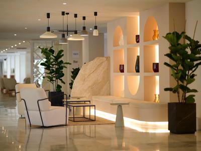 Elegantní hotelová hala s křesly, rostlinami a teple osvětlenými policemi.