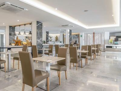 Moderní, světlá hotelová restaurace se šedými židlemi a bílými stoly na mramorové podlaze.