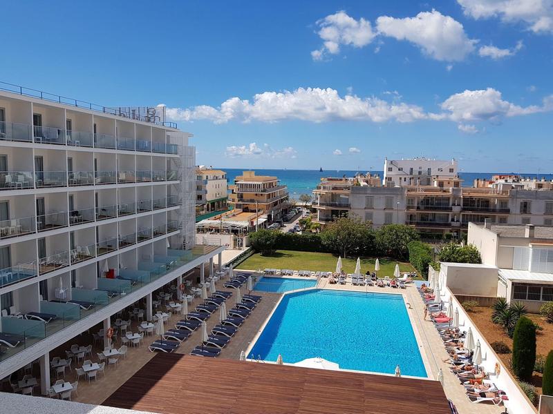 Hotel con grande piscina, lettini e vista sul mare sotto un cielo soleggiato.