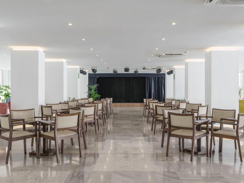 Sala eventi moderna e luminosa con file di sedie e palco in fondo.