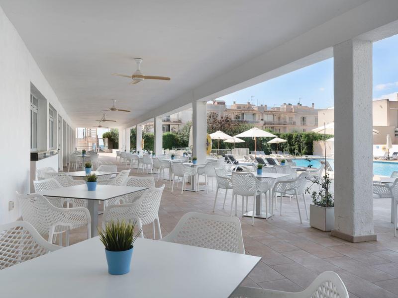 Terrazza coperta con tavoli e sedie bianchi accanto a una piscina dell'hotel.