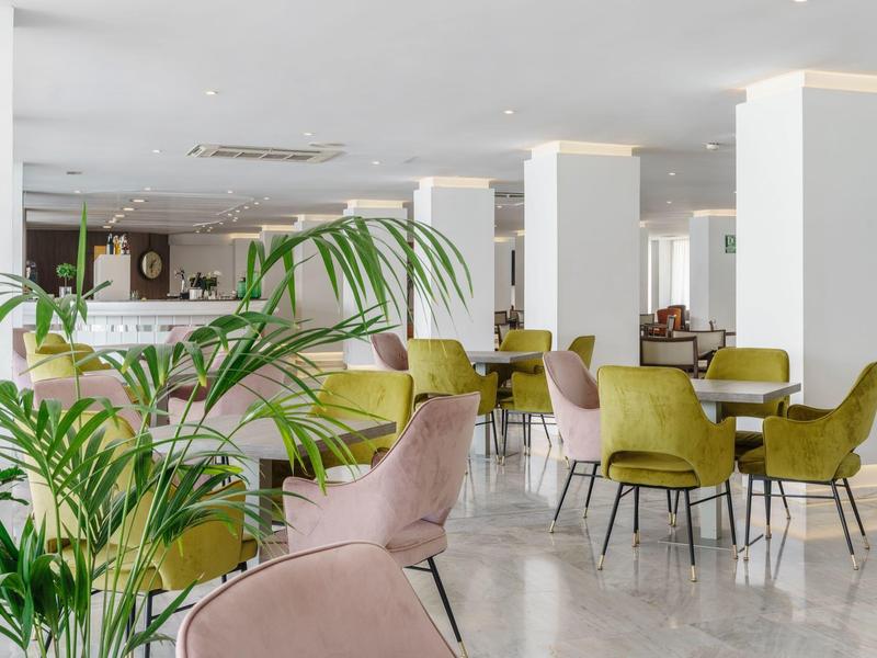 Lounge dell'hotel luminosa con sedie moderne, tavoli e piante in uno spazio aperto.