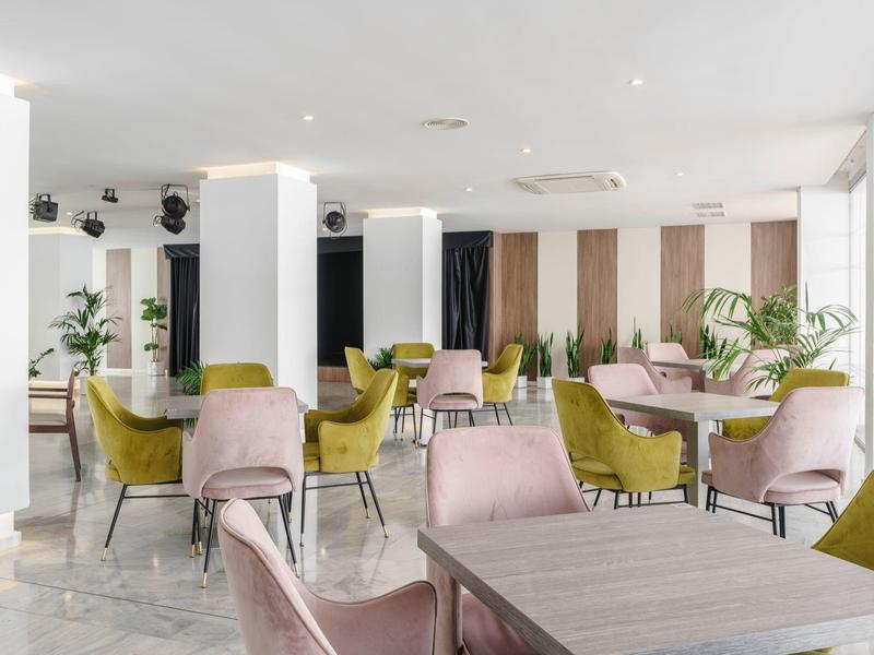 Zona pranzo luminosa e moderna con sedie rosa e verdi e piante come decorazione.