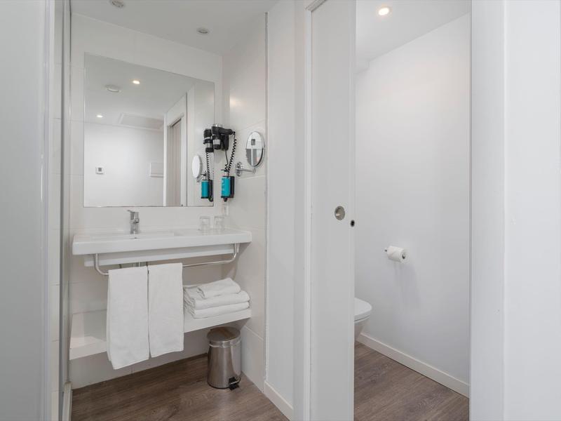 Bagno moderno con lavabo, specchio, asciugamani e WC separato.