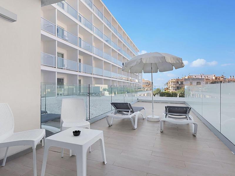 Balcone moderno con sedie a sdraio, tavolo e sedia, ringhiera in vetro, vista sulla città e sul mare.