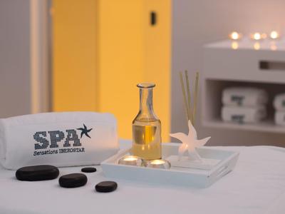 Nahaufnahme eines Spa-Setups mit Handtuch, Duftöl, Muschel, Stäbchen und schwarzen Steinen.