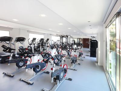 Bright gym with multiple stationary bikes and treadmills next to large windows.