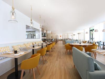 Helles, modernes Café mit Holzfußboden, gelben Stühlen und Sitzbank entlang der Wand.