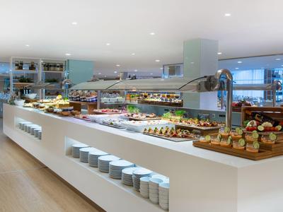 Moderne Buffetinsel mit vielfältigem Frühstücksangebot, helle Einrichtung, klare Linien und große Fenster.