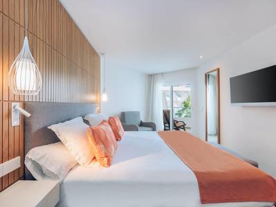 Modernes helles Schlafzimmer mit Doppelbett, Holzwand, orangen Decken und großem Fenster.