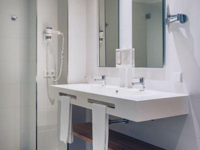 Modernes Badezimmer mit weißem Waschtisch, großen Spiegeln, Haartrockner und grauem Fliesenboden.