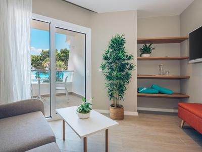 Helles Wohnzimmer mit Sofa, Couchtisch, großem Pflanzenkübel und Balkon mit Poolblick.