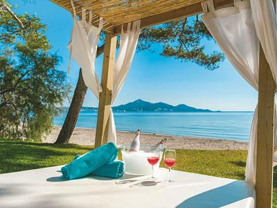 Sunny beach view with a cozy pavilion, two wine glasses, and turquoise decor.