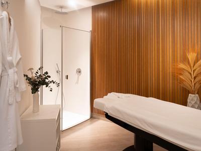 Elegancki pokój spa z łóżkiem do masażu, drewnianą ścianą i ciepłym oświetleniem.