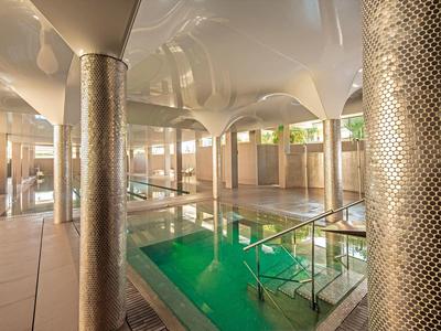 Innenbereich eines Schwimmbads mit Säulen, grünem Wasserbecken und warmem Licht.