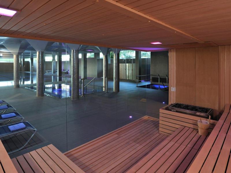 Geräumiger Saunaraum mit Holzverkleidung, großen Spiegeln und blauen Auflagen auf Holzbänken.