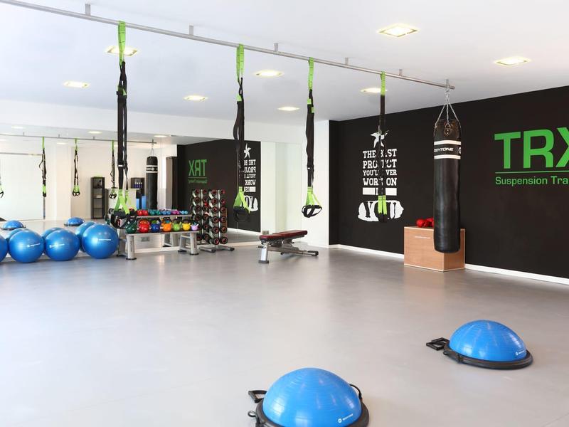 Moderne Fitnessraum mit TRX-Bändern, blauen Gymnastikbällen und Hanteln an weißen Wänden.