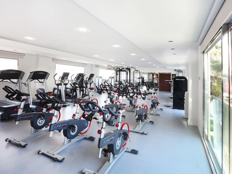 Moderne Fitnesshalle mit Spinning-Rädern, Laufbändern und großem Fenster für viel Tageslicht.