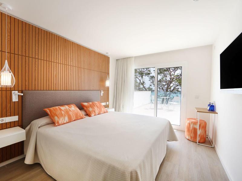 Helles Schlafzimmer mit Doppelbett, Holzwand, weißen Wänden und Fenster mit Baum-Blick.