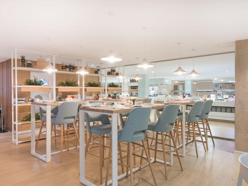 Heller, moderner Essbereich mit blauen Stühlen, Holztischen und mehreren Hängeleuchten.