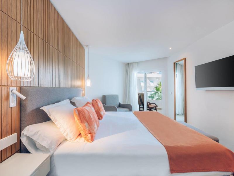 Modernes helles Schlafzimmer mit Doppelbett, Holzwand, orangen Decken und großem Fenster.