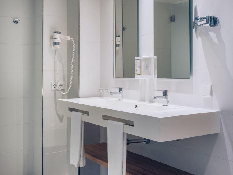 Modernes Badezimmer mit weißem Waschtisch, großen Spiegeln, Haartrockner und grauem Fliesenboden.