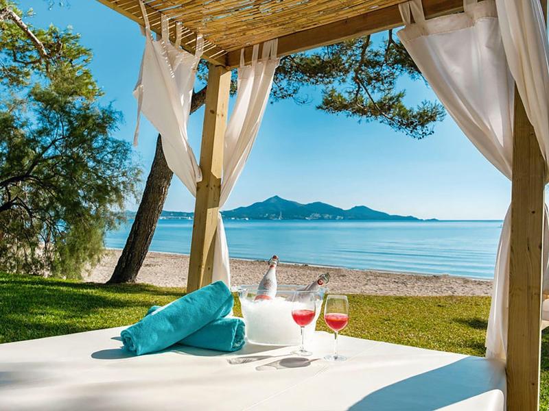 Strand mit Pavillon, türkisfarbenes Handtuch, zwei Cocktails, blauer Himmel und ruhiges Meer im Hintergrund.