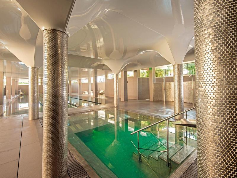 Innenbereich eines Schwimmbads mit Säulen, grünem Wasserbecken und warmem Licht.